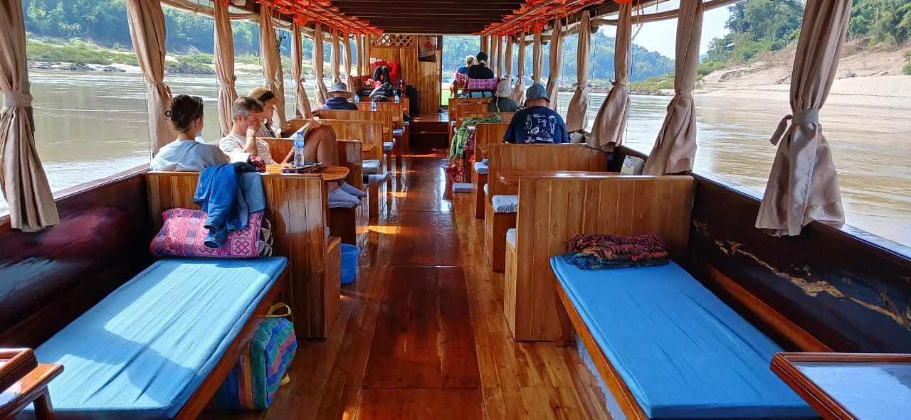 Wooden cabin with blue cushions, passengers looking out at the river